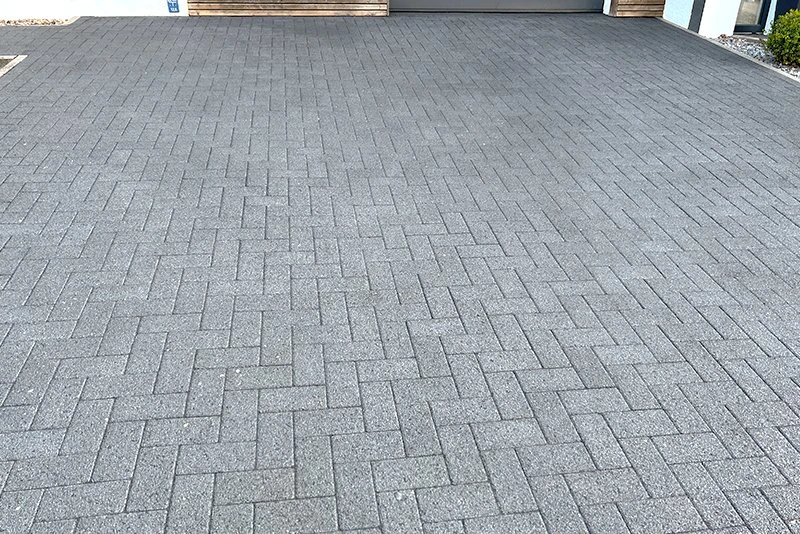 Gepflasterte Einfahrt mit grauen rechteckigen Betonsteinen im Fischgrätmuster vor Garage.